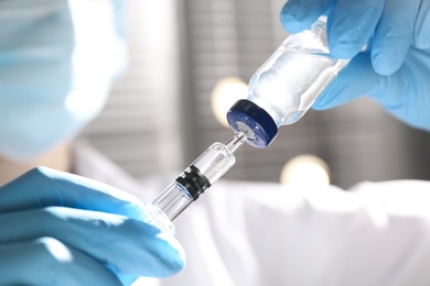 Woman filling syringe with vaccine from vial on blurred background, closeup