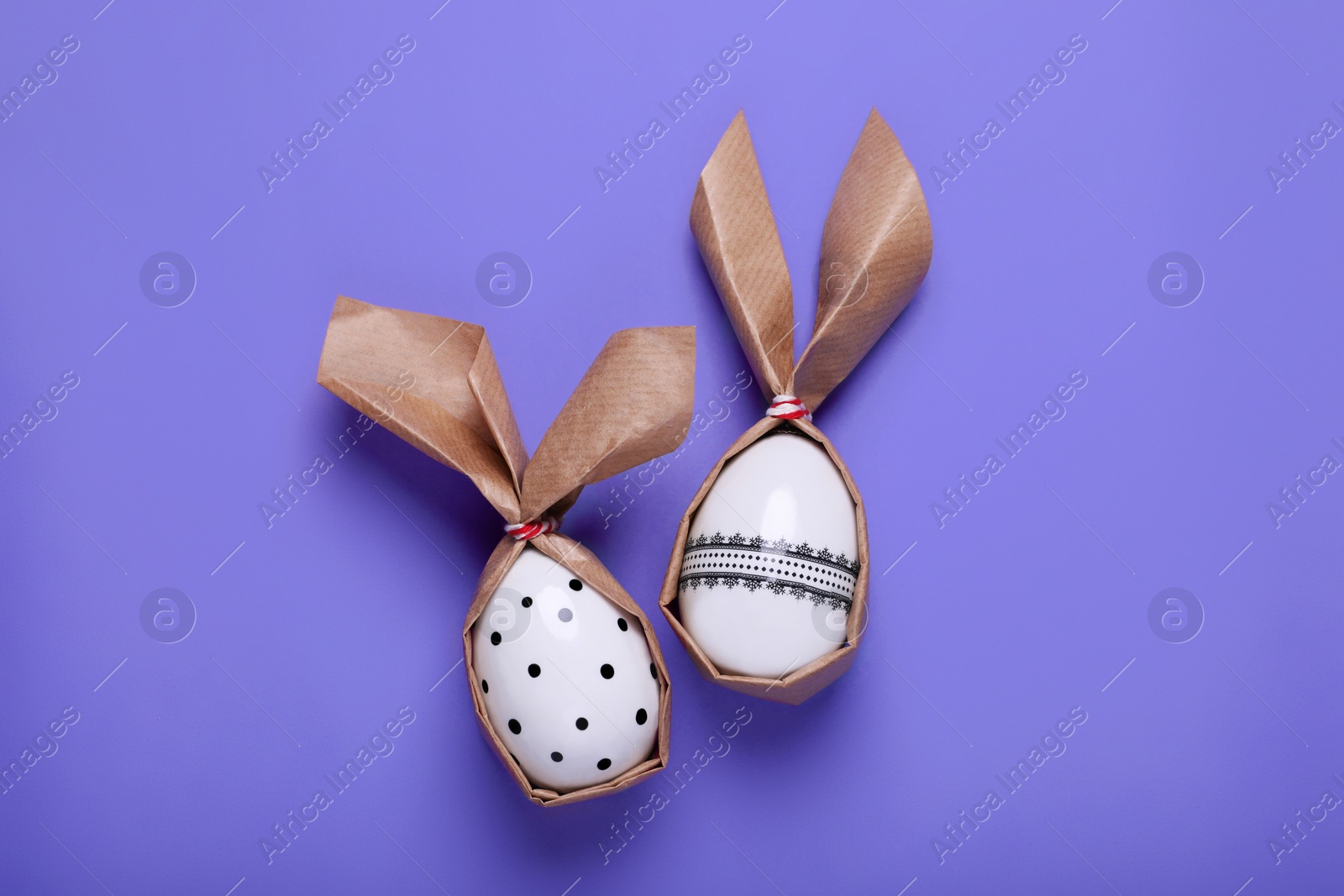 Photo of Easter bunnies made of craft paper and eggs on purple background, flat lay