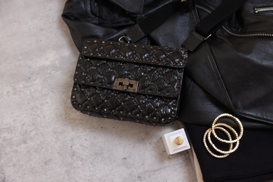 Bag, black leather jacket, bottle of perfume and golden bracelets on grey table, flat lay. Space for text