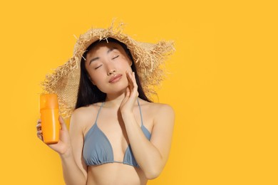 Photo of Beautiful young woman in straw hat holding sun protection cream on orange background, space for text