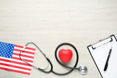 Photo of Stethoscope, red heart, clipboard and American flag on white wooden table, flat lay. Space for text