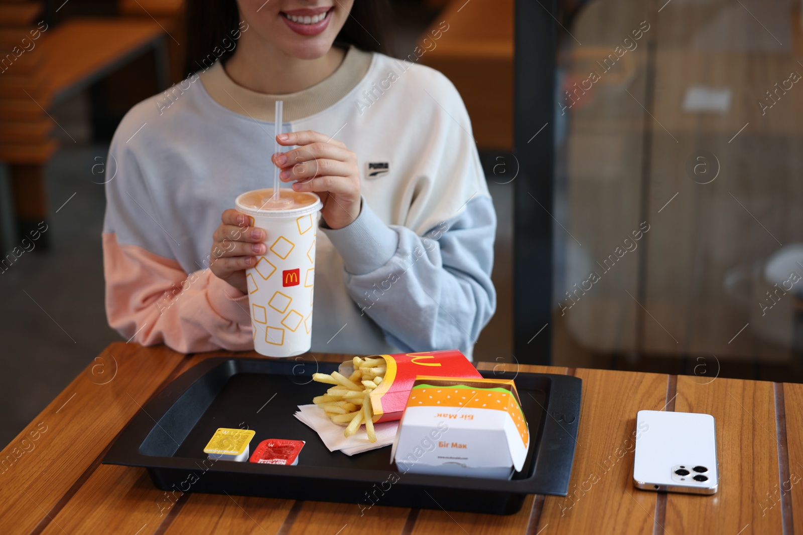 Photo of Lviv, Ukraine - September 26, 2023: Woman with McDonald's drink, burger and french fries at wooden table in restaurant, closeup