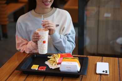 Photo of Lviv, Ukraine - September 26, 2023: Woman with McDonald's drink, burger and french fries at wooden table in restaurant, closeup