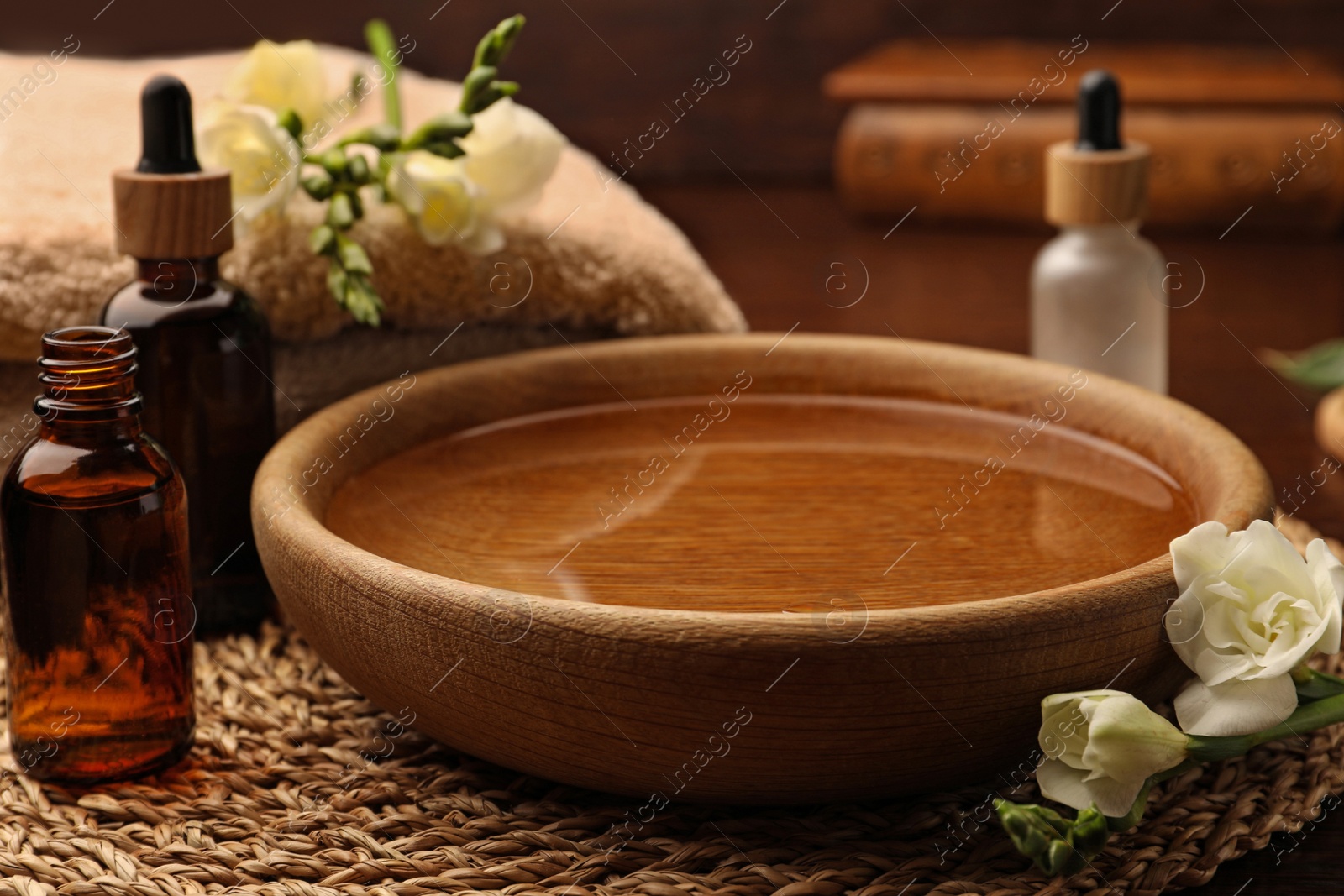 Photo of Bowl of water, bottles with essential oil and beautiful roses on table. Aromatherapy treatment