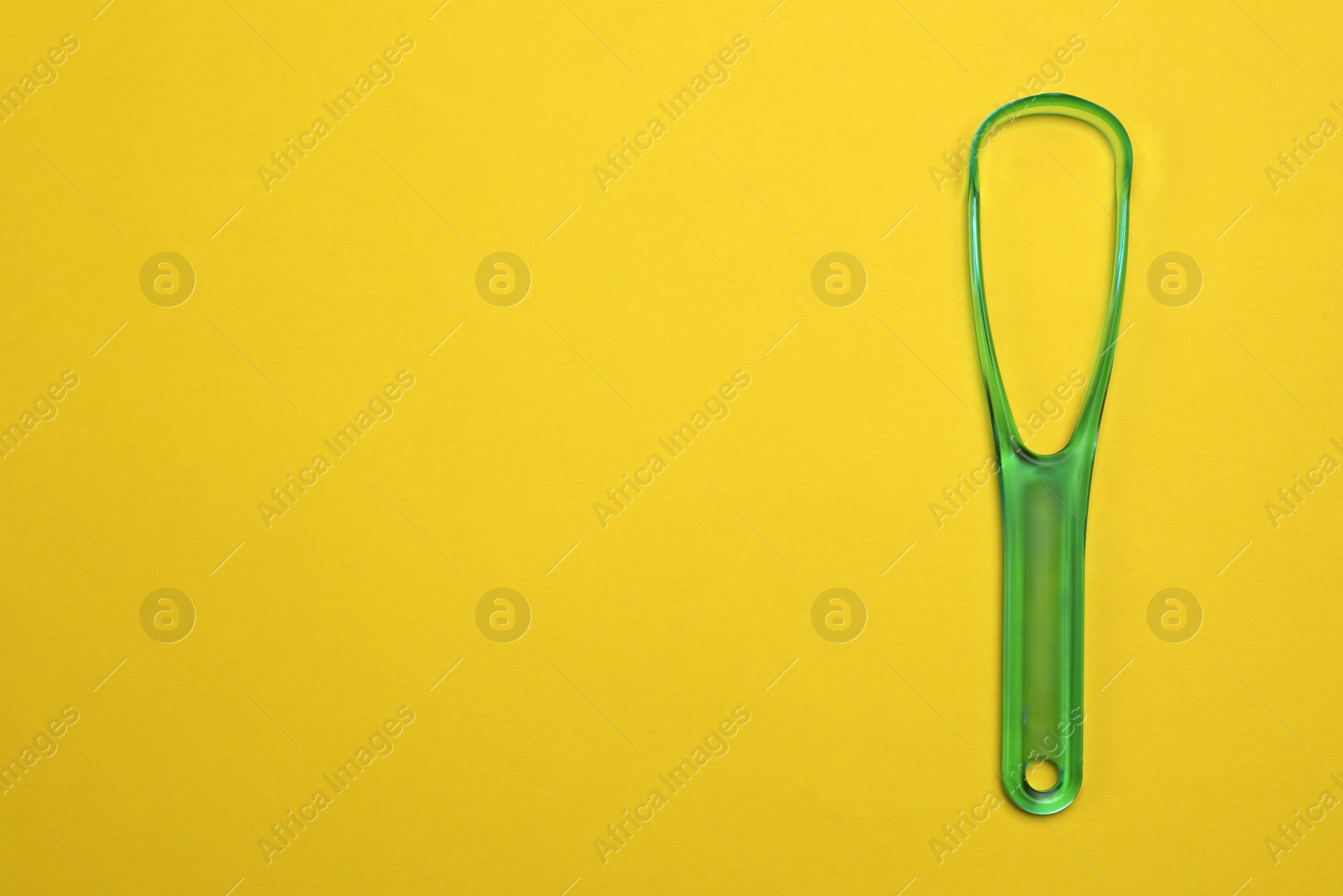 Photo of Green tongue cleaner on yellow background, top view. Space for text