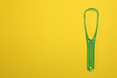 Photo of Green tongue cleaner on yellow background, top view. Space for text