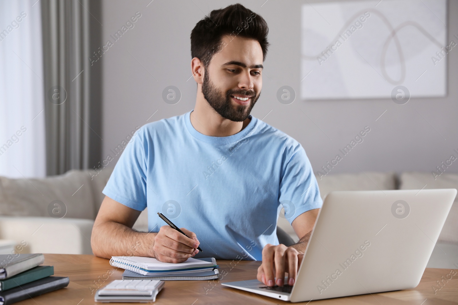 Photo of Young man watching webinar at table in room