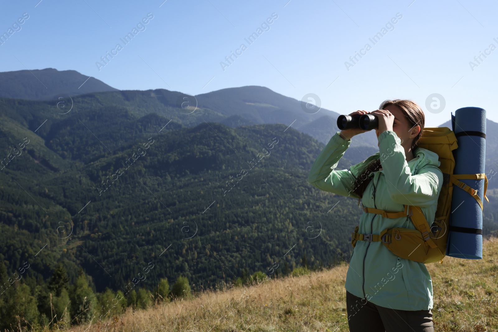 Photo of Tourist with backpack and sleeping pad looking through binoculars in mountains