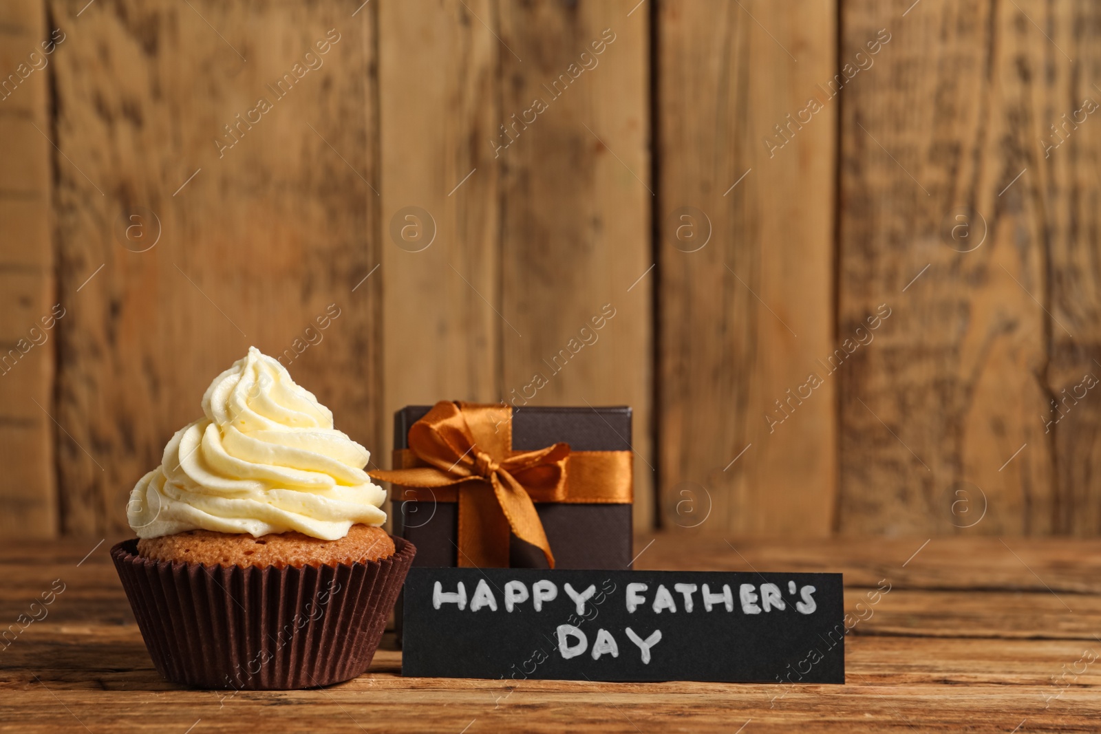 Photo of Card with phrase HAPPY FATHER'S DAY, tasty cupcake and gift box on wooden background