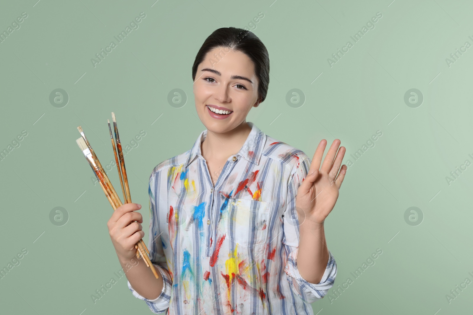 Photo of Woman with paintbrushes on pale green background. Young artist