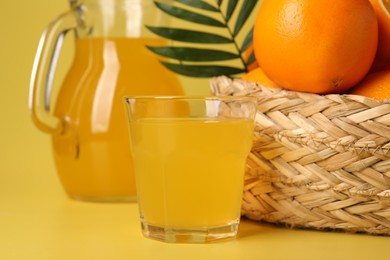 Photo of Fresh oranges in wicker basket and juice on yellow background, closeup