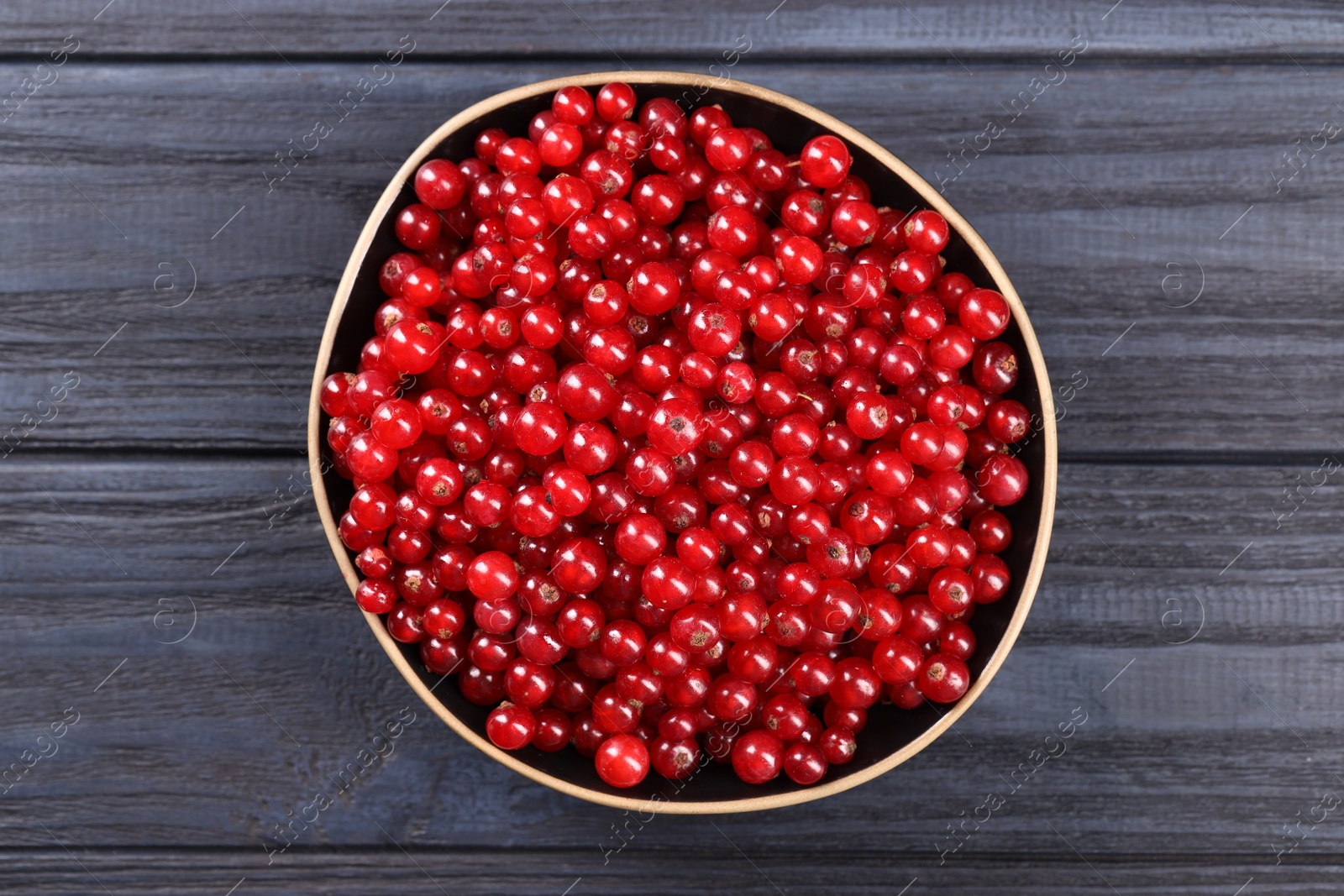 Photo of Ripe red currants in bowl on wooden rustic table, top view