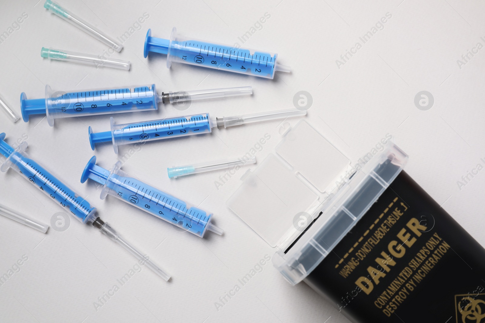 Photo of Disposable syringes, needles and sharps container on light background, flat lay