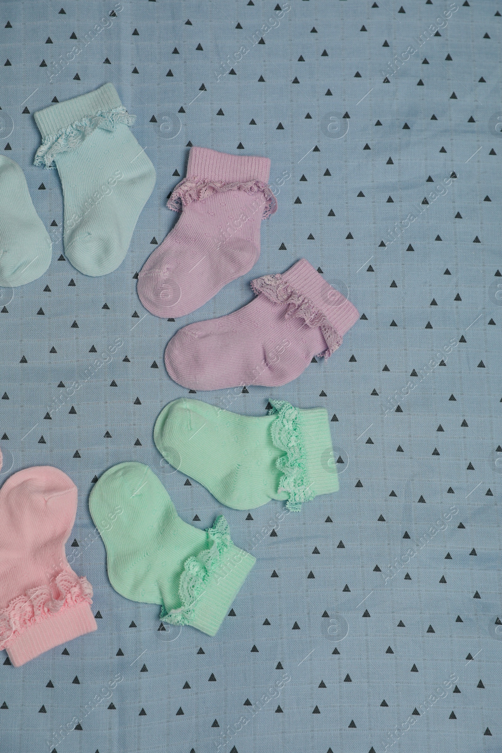 Photo of Many colorful baby socks on light blue fabric, flat lay