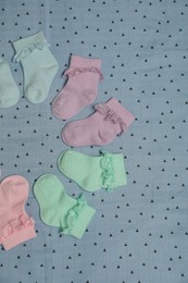 Many colorful baby socks on light blue fabric, flat lay