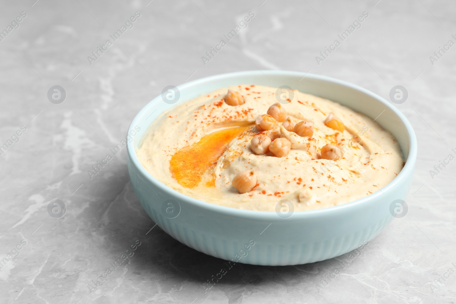 Tasty hummus with garnish in bowl on light grey marble table Photo of Tasty hummus with garnish in bowl on light grey marble table
