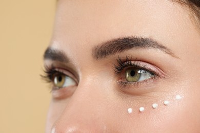 Young woman with cream around eye on beige background, closeup