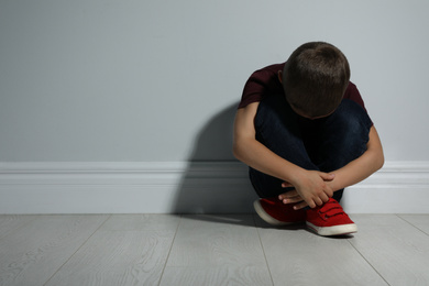 Little boy near white wall, space for text. Domestic violence concept