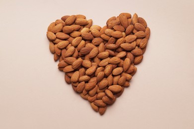 Photo of Heart made of delicious raw almonds on beige background, flat lay