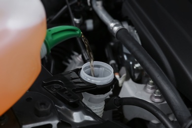 Photo of Pouring liquid from plastic canister into car washer fluid reservoir, closeup