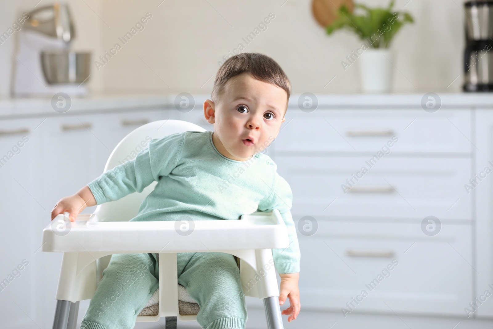 Photo of Cute little baby sitting in high chair at kitchen. Space for text