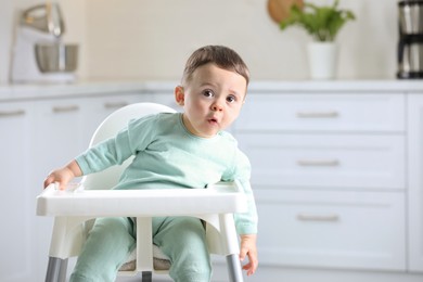 Cute little baby sitting in high chair at kitchen. Space for text