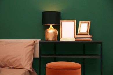 Photo of Table with lamp, books and empty frames near bed indoors. Interior design
