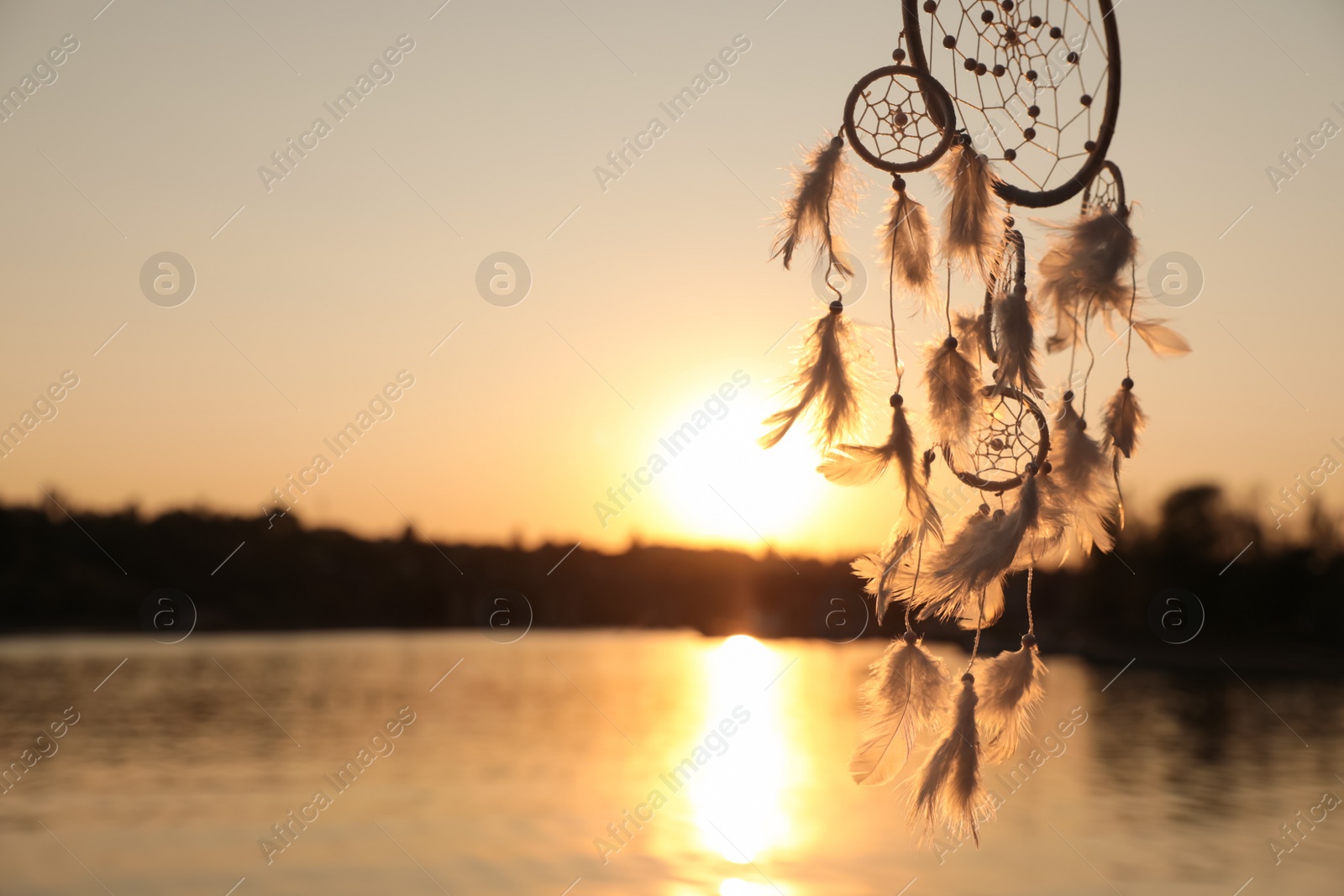 Photo of Beautiful handmade dream catcher near river at sunset. Space for text