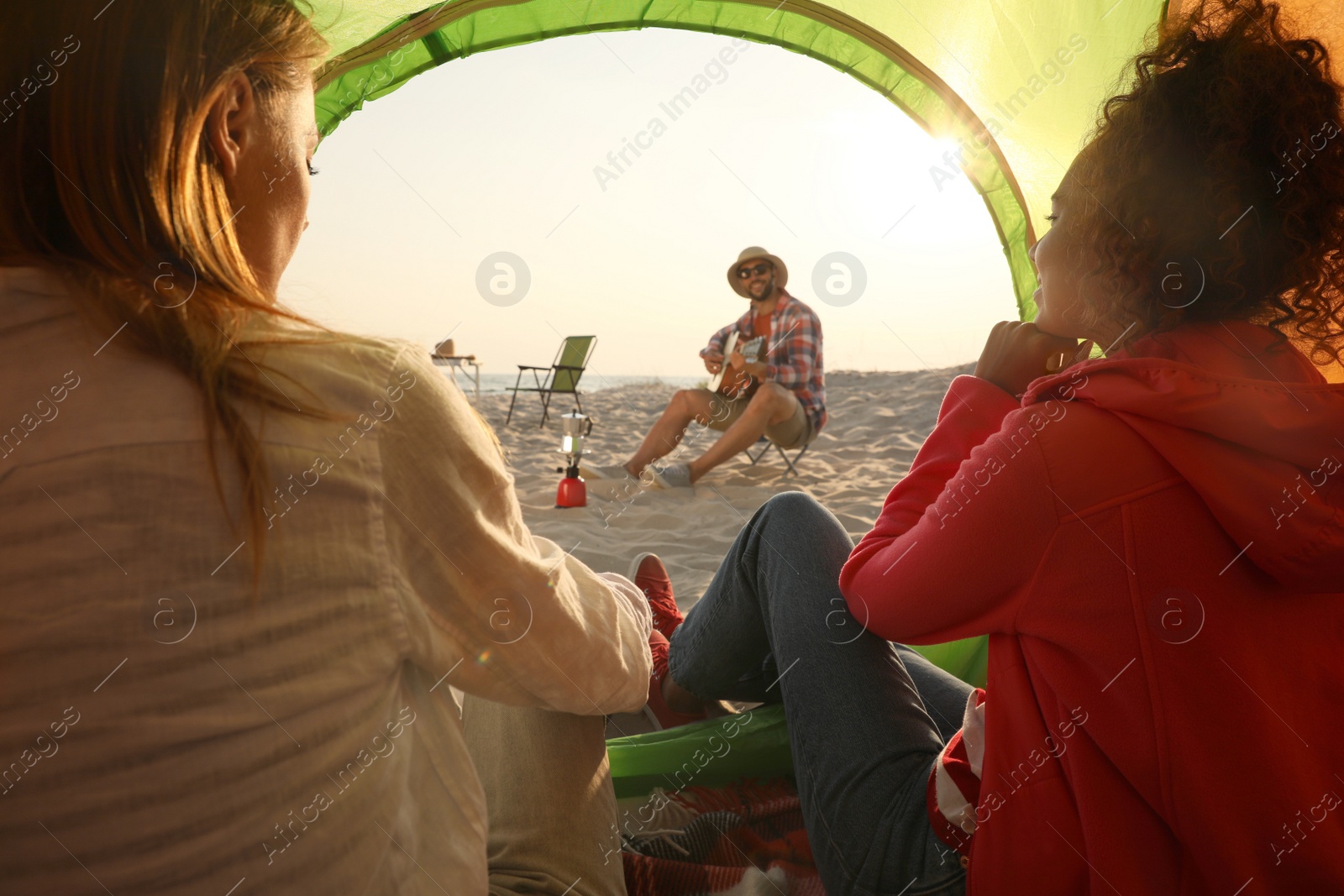 Photo of Friends resting on sandy beach. View from camping tent