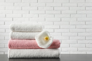 Photo of Stack of folded soft towels with flower on table near brick wall. Space for text