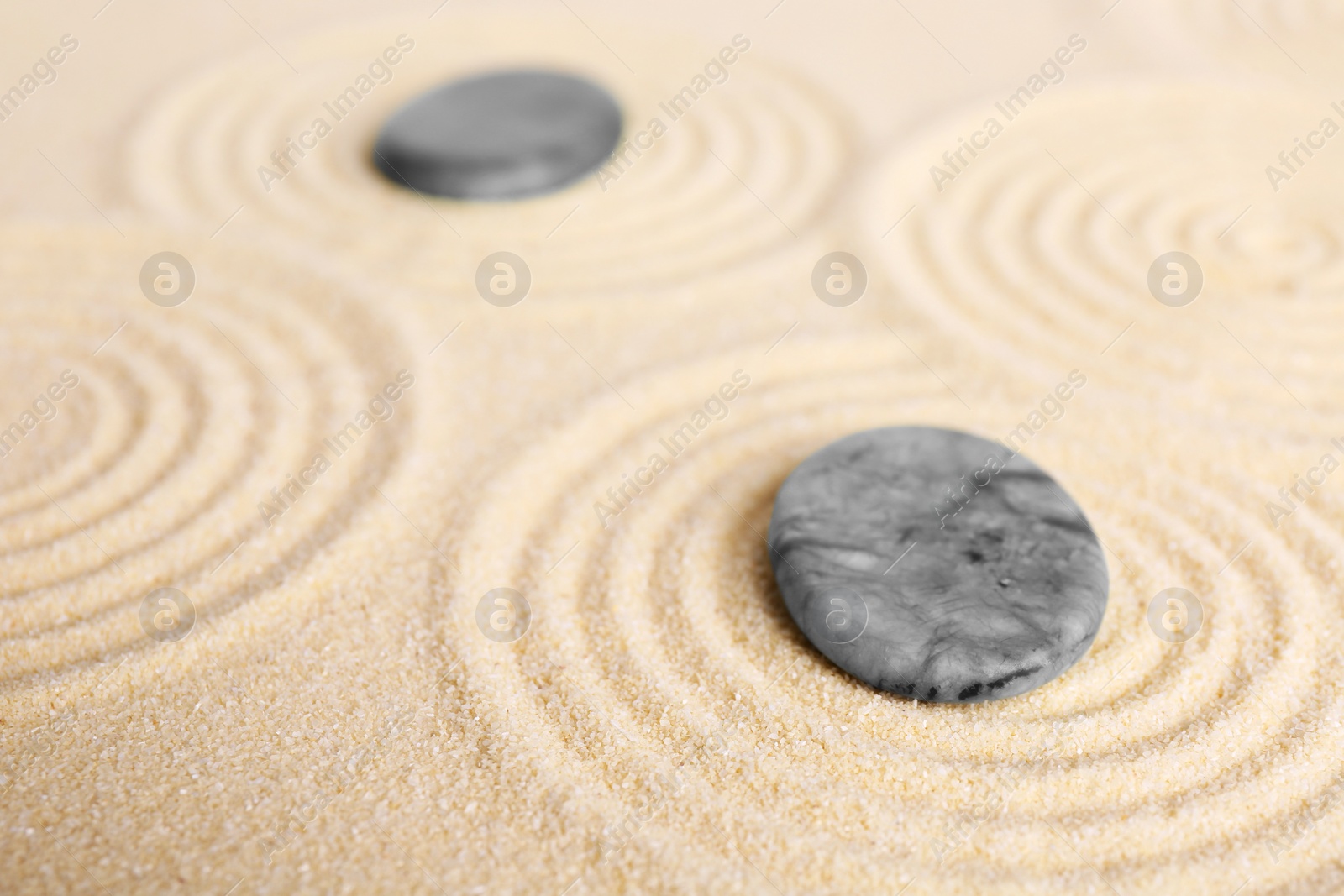 Photo of Zen garden stones on beige sand with pattern, closeup