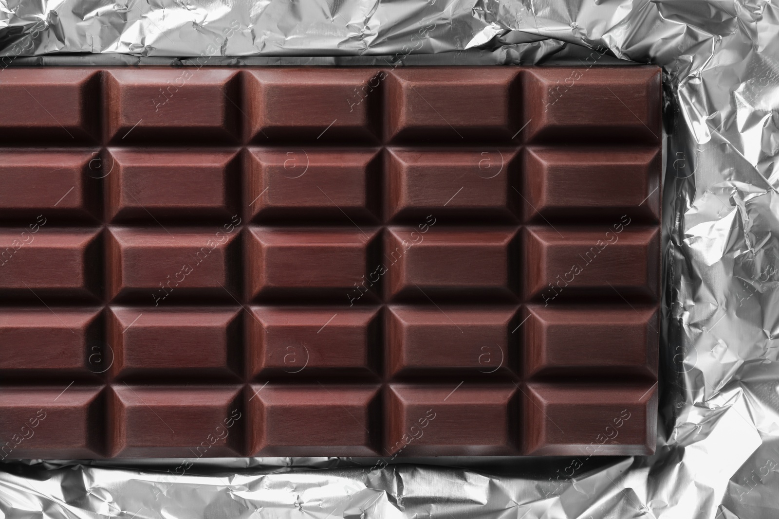 Photo of Delicious dark chocolate bar on foil, top view