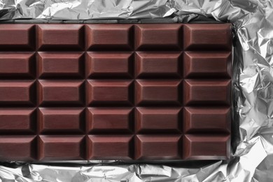 Delicious dark chocolate bar on foil, top view