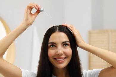 Photo of Beautiful woman applying hair serum in bathroom. Cosmetic product