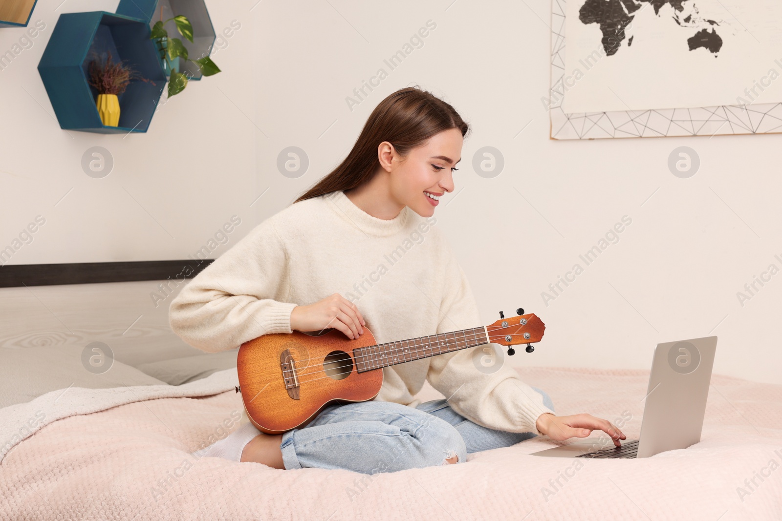 Photo of Happy young woman learning to play ukulele with online music course at home. Time for hobby