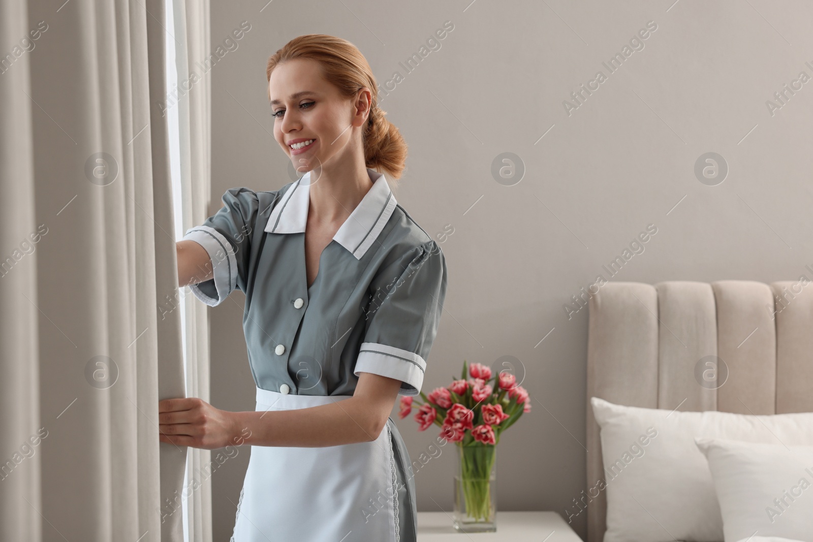 Photo of Chambermaid opening window curtains in hotel bedroom