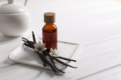 Photo of Vanilla pods, essential oil and flowers on white wooden table, space for text