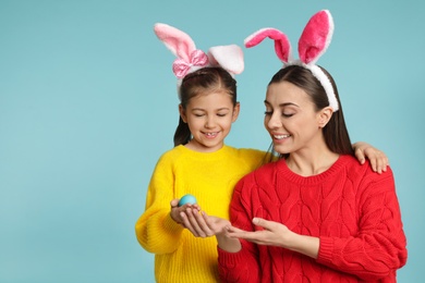 Daughter showing Easter egg to her mother on color background, space for text