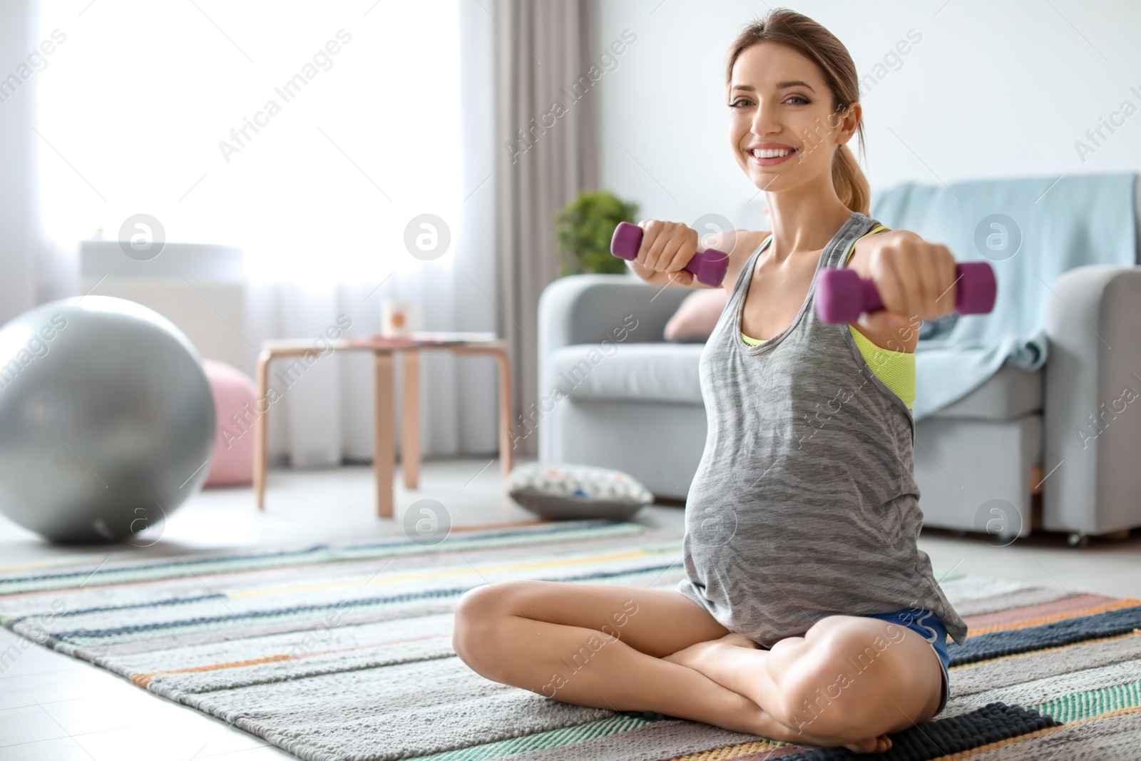 Photo of Young pregnant woman doing exercises with dumbbells at home