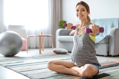 Young pregnant woman doing exercises with dumbbells at home