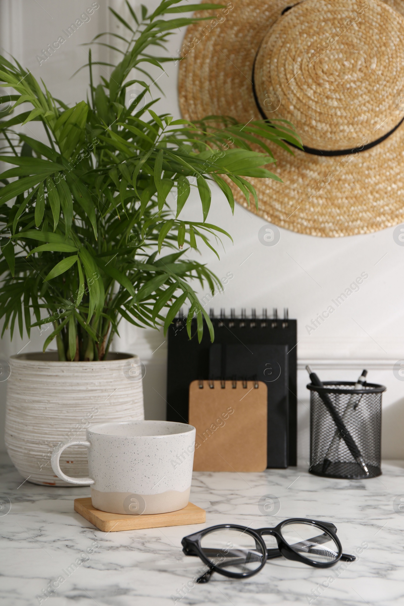 Photo of Stylish office workplace. Decor elements, glasses, cup and stationery on marble table near white wall