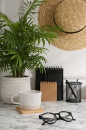 Photo of Stylish office workplace. Decor elements, glasses, cup and stationery on marble table near white wall