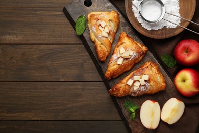 Fresh tasty puff pastry with sugar powder, mint and apples served on wooden table, flat lay. Space for text