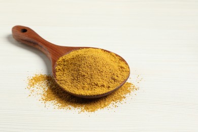 Photo of Curry powder in spoon on white wooden table. Space for text