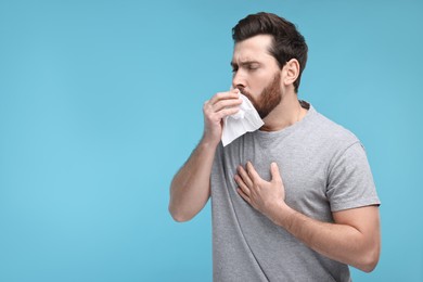 Photo of Sick man with tissue coughing on light blue background, space for text