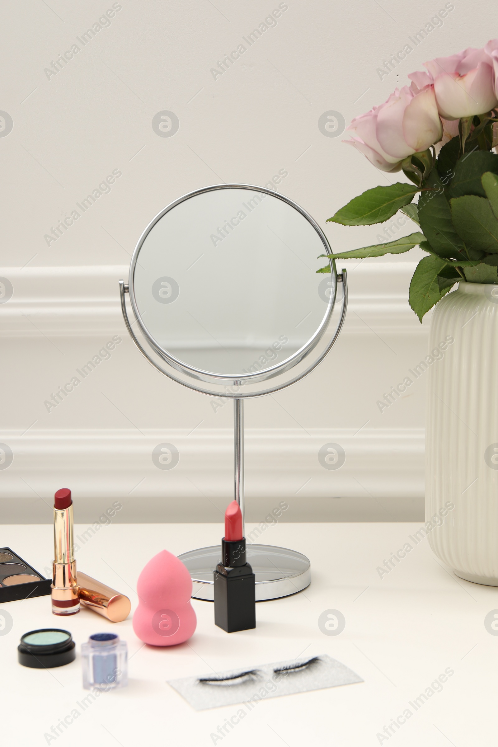 Photo of Mirror, cosmetic products and vase with pink roses on white dressing table