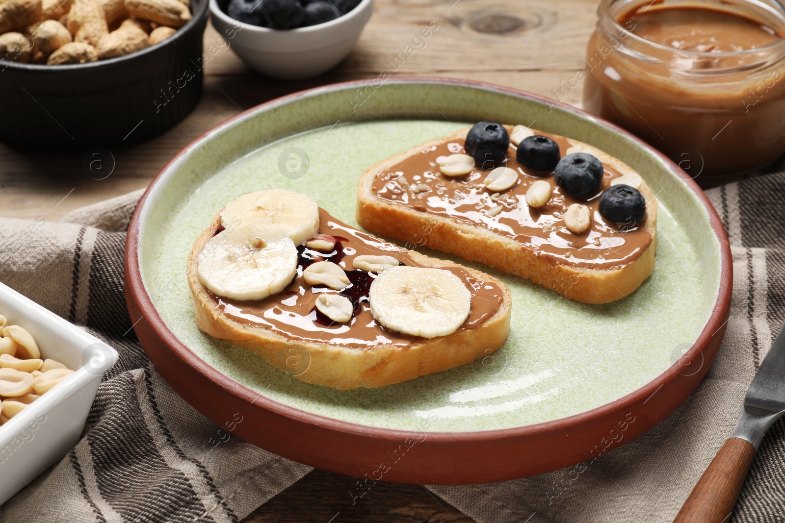 Photo of Toasts with tasty nut butter, banana slices, blueberries and peanuts on table, closeup