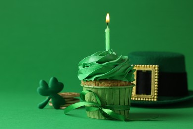 Photo of St. Patrick's day party. Tasty cupcake with burning candle and leprechaun hat on green background, closeup