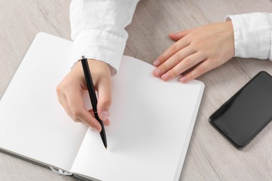 Photo of Woman writing in notebook at wooden table, closeup