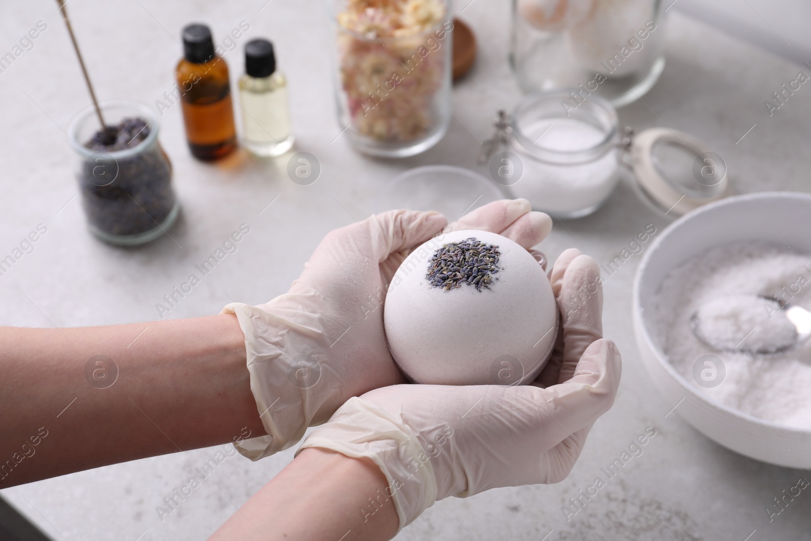 Photo of Woman in gloves with self made bath bomb at grey table, closeup